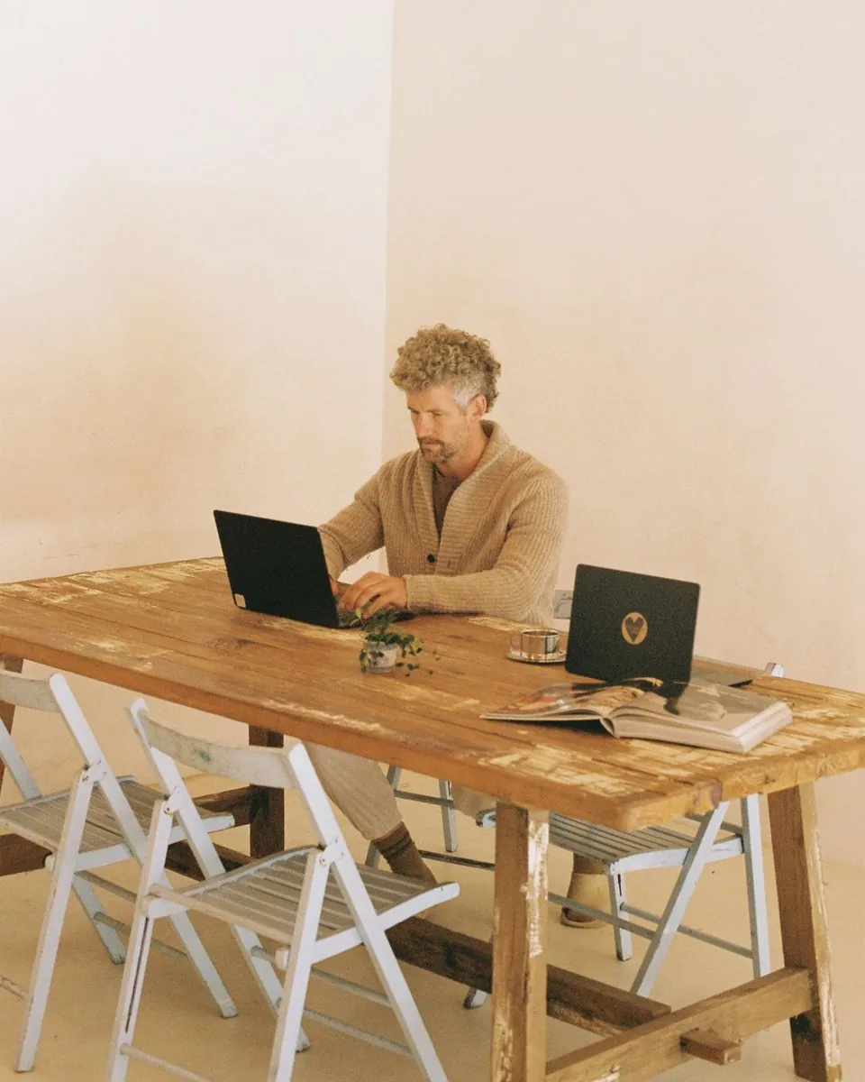A member working on a laptop at the Bali table, built from an old wooden boat, with white folding chairs around it