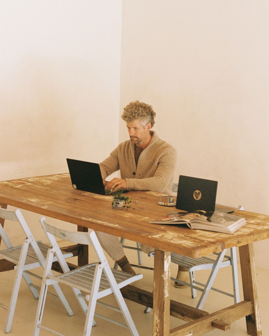 A member working on a laptop at the Bali table, built from an old wooden boat, with white folding chairs around it